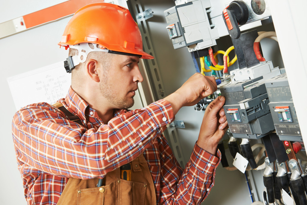 An electrician wearing an orange hard hat while screwing an equipment to a fuse box