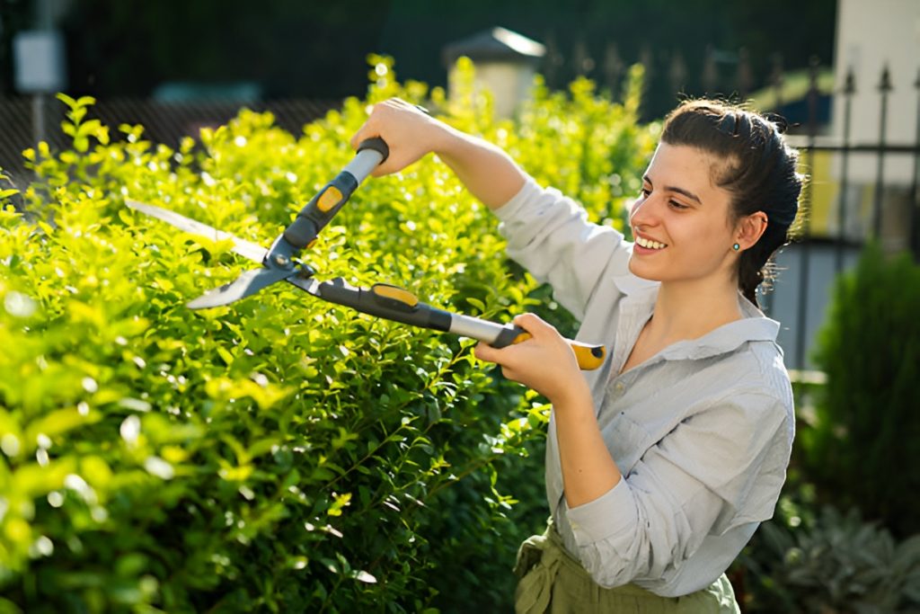 smiling woman trimming bushes in the front yard